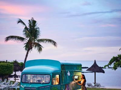 Grüner Vintage-Bus neben Palme am Strand bei Sonnenuntergang mit Person darin.