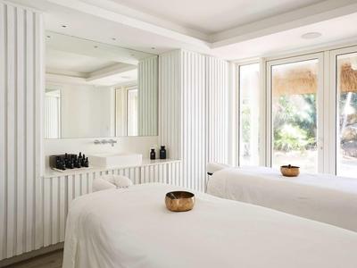 Lichte spakamer met twee massagetafels, grote ramen en minimalistische inrichting.