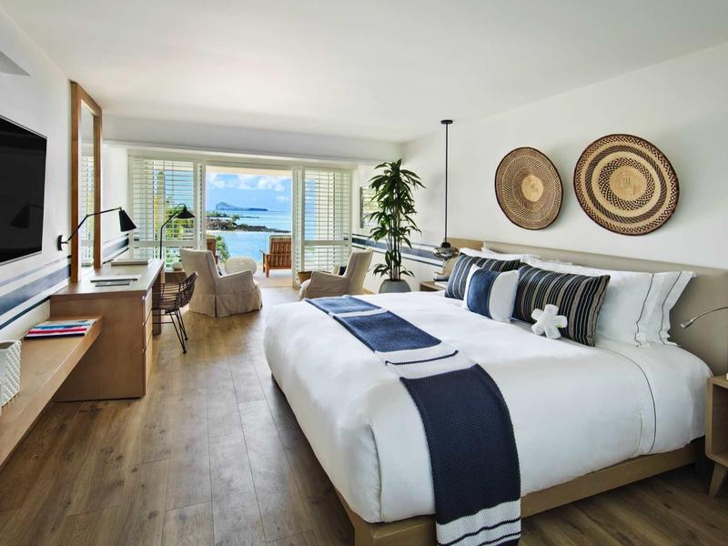 Lichte hotelkamer met groot bed, houten vloer en balkon met zeezicht.