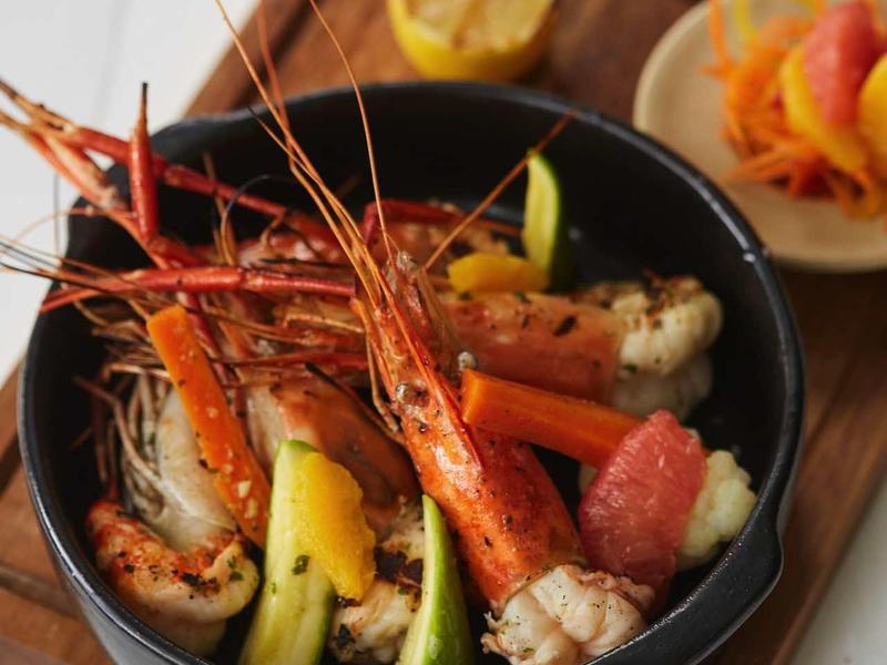 Kom met gegrilde garnalen, groenten en citroen geserveerd op een houten plank.