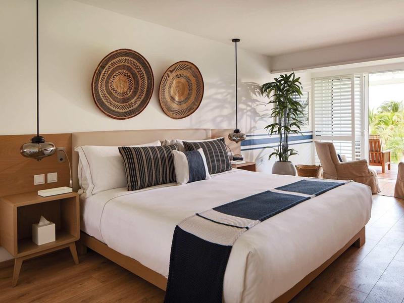 Moderne hotelkamer met groot bed, decoratieve kussens, houten meubels en toegang tot een terras.