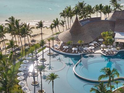 Luxuriöser Poolbereich mit Liegestühlen und Palmen am Strand.