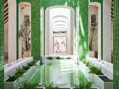 Heller Innenhof mit grün gefliesten Wänden, Wasserbecken und weißen Sitzbänken unter Bögen.