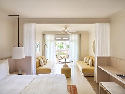 Helles Hotelzimmer mit Doppelbett, Sitzbereich mit Sofas und Blick auf Terrasse mit Garten.