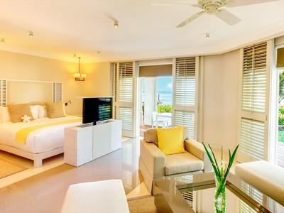 Helles Hotelzimmer mit gemütlichem Bett, Balkon und Blick auf tropische Palmen und das Meer.