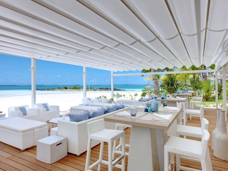 Plážový salon s bílým moderním nábytkem s výhledem na moře a modrou oblohu.