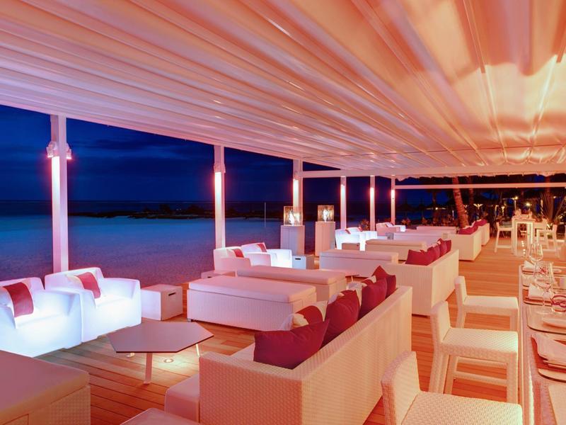 Moderní venkovní terasa s pohovkami a stoly s výhledem na moře za soumraku.