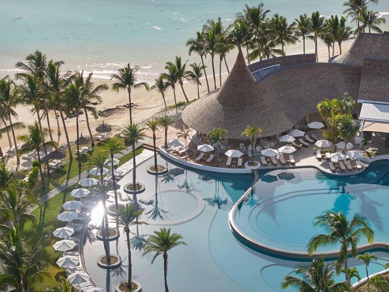 Luxusní bazénová plocha s lehátky a palmami u pláže.