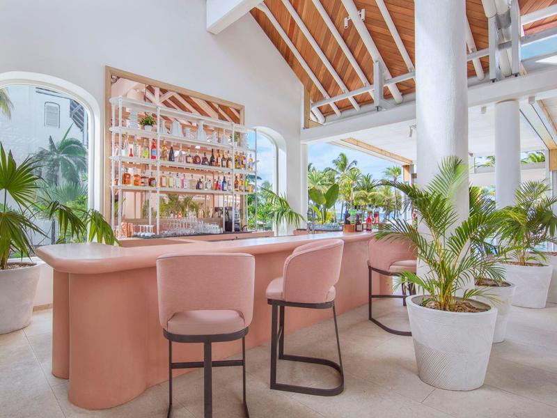 Moderní otevřená odpočinková zóna s růžovým barem, židlemi a mnoha zelenými rostlinami.