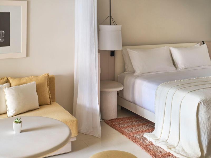 Moderní hotelový pokoj s velkou postelí, pohovkou a kulatým stolkem v neutrálních barvách.