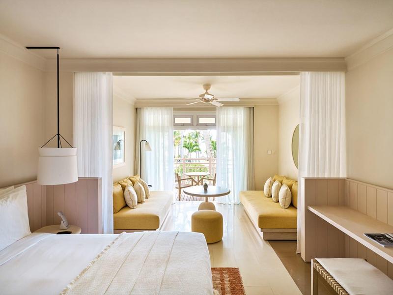 Světý hotelový pokoj se dvěma posezeními, postelí a přístupem na terasu.