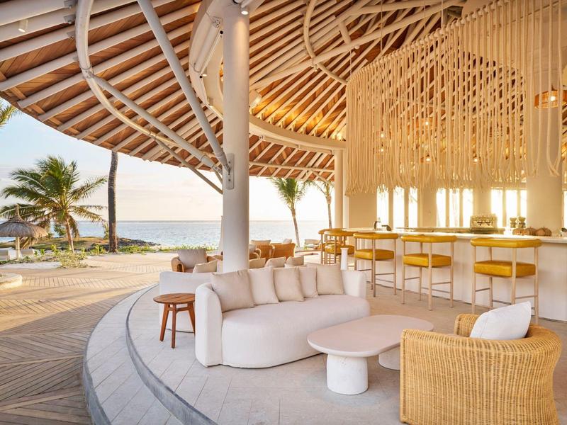 Otevřená relaxační zóna s moderním posezením a barem, výhled na moře a palmy.