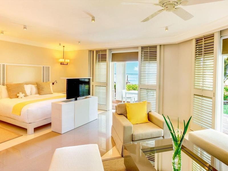 Světý hotelový pokoj s postelí, posezením a výhledem na moře skrz okna.