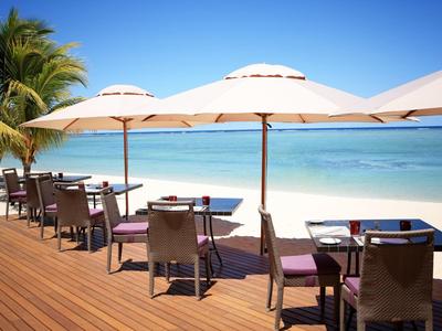 Terras met tafels en stoelen onder parasols op een strand met palmbomen en blauwe zee