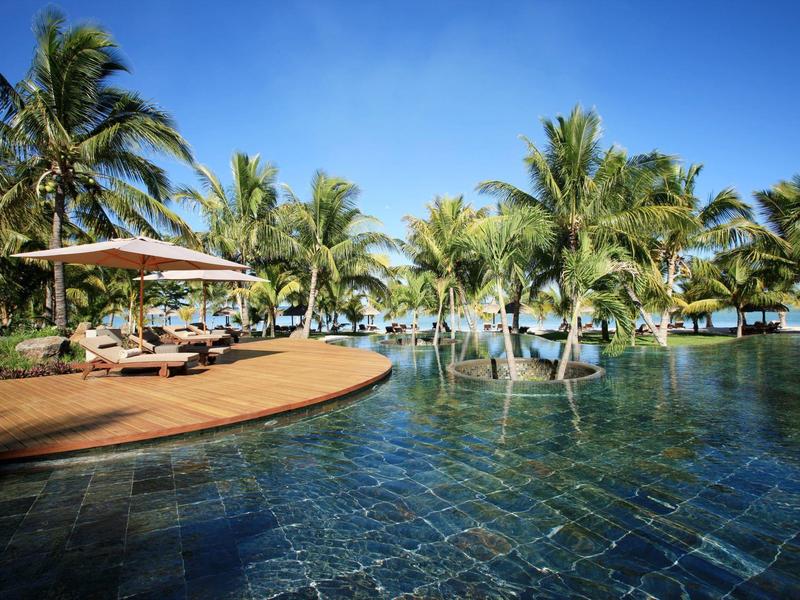 Luxe zwembad met palmbomen en ligstoelen onder een heldere blauwe lucht.