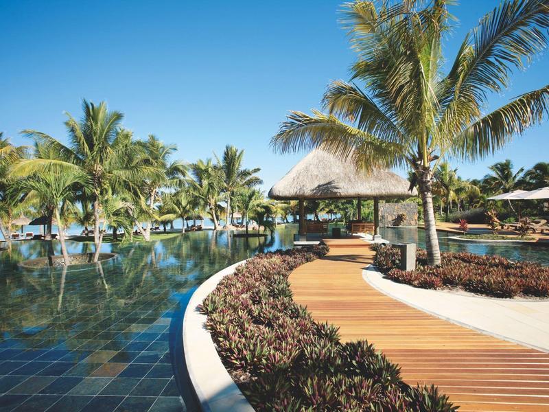 Een tropisch resortzwembad met palmbomen en een houten pad onder een blauwe lucht.