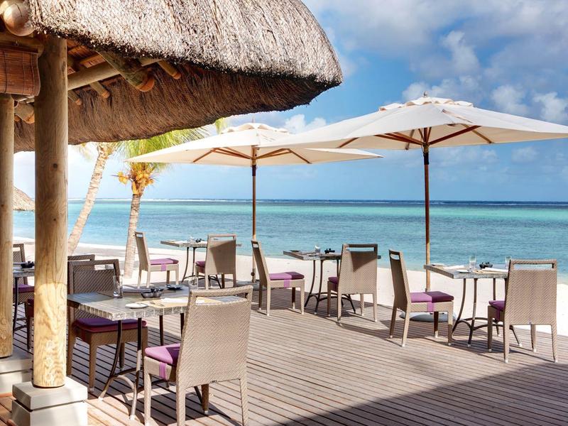 Strandbar met tafels en stoelen onder parasols direct aan zee.