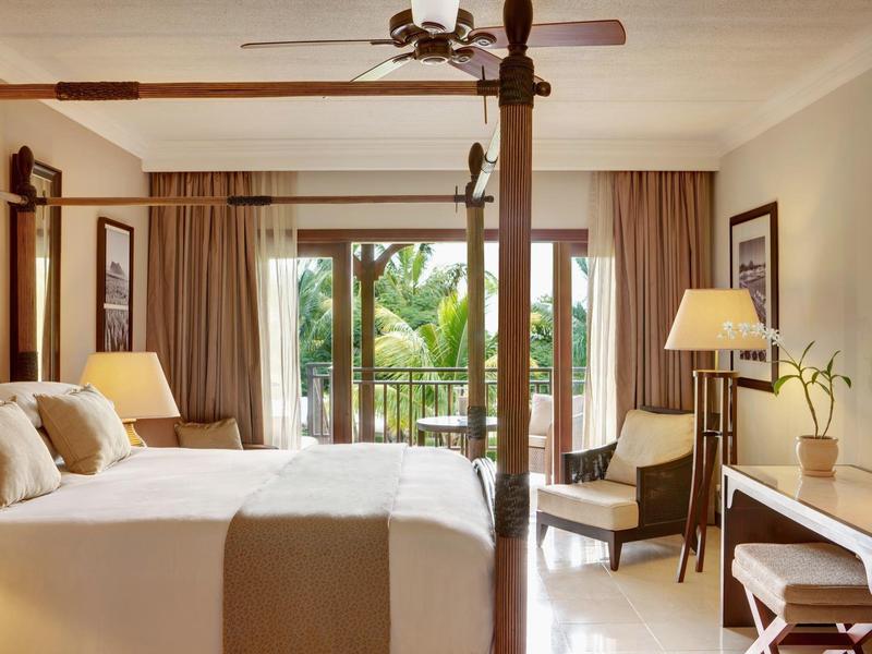 Lichte slaapkamer met tweepersoonsbed, plafondventilator en uitzicht op tropische tuin.