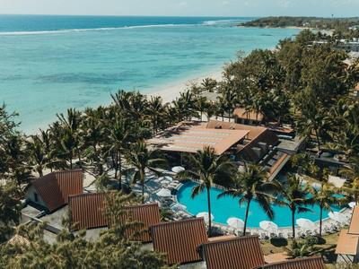 Luxuriöses Resort mit Pool und Palmen direkt am Strand mit Blick auf das blaue Meer.