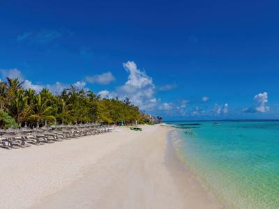 Weißer Sandstrand mit Liegestühlen, Palmen und klarem blauem Wasser unter blauem Himmel.