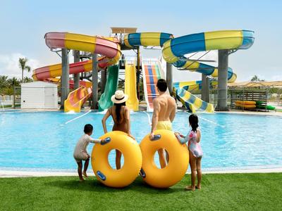 Familie mit Schwimmreifen blickt auf große bunte Wasserrutschen im Freibad.