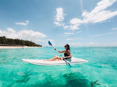 Frau paddelt auf einem Kajak in klarem, türkisfarbenem Meer nahe einem Sandstrand.
