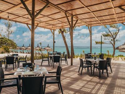 Offenes Restaurant mit Meerblick, Stühlen und Tischen unter einem Holzdach am Strand.