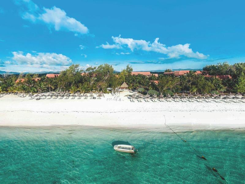 Wit zandstrand met ligbedden, parasols en een kleine boot in helder turquoise water.