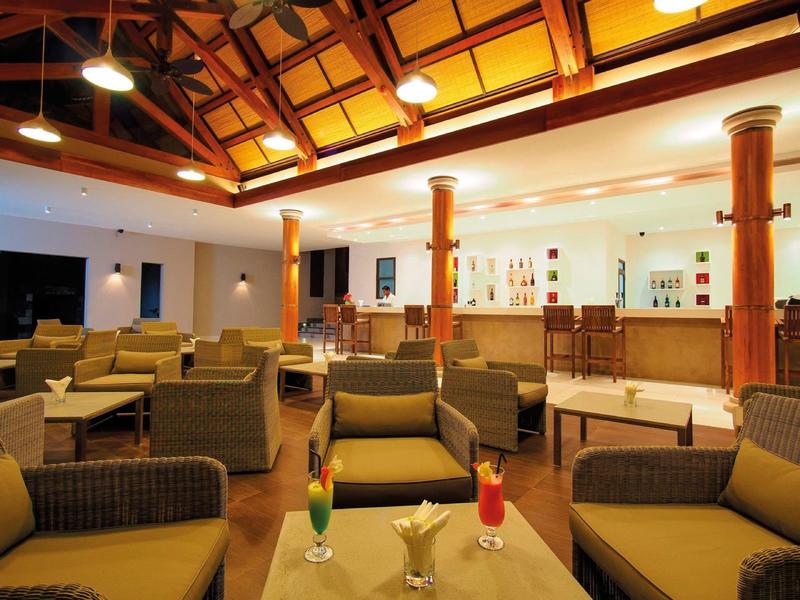 Ruime hotel lounge met rotan banken, houten plafond en bar met kleurrijke drankjes.