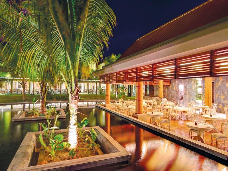 Buiten eetgedeelte bij water met palmbomen 's nachts, warme verlichting en rustige sfeer