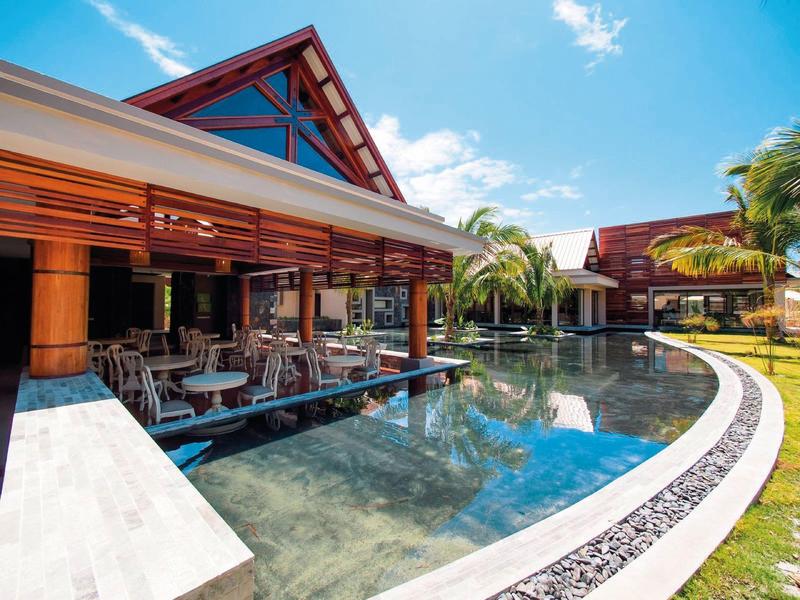 Eetgelegenheid bij het zwembad met houten constructies en tropische palmbomen onder een blauwe hemel.