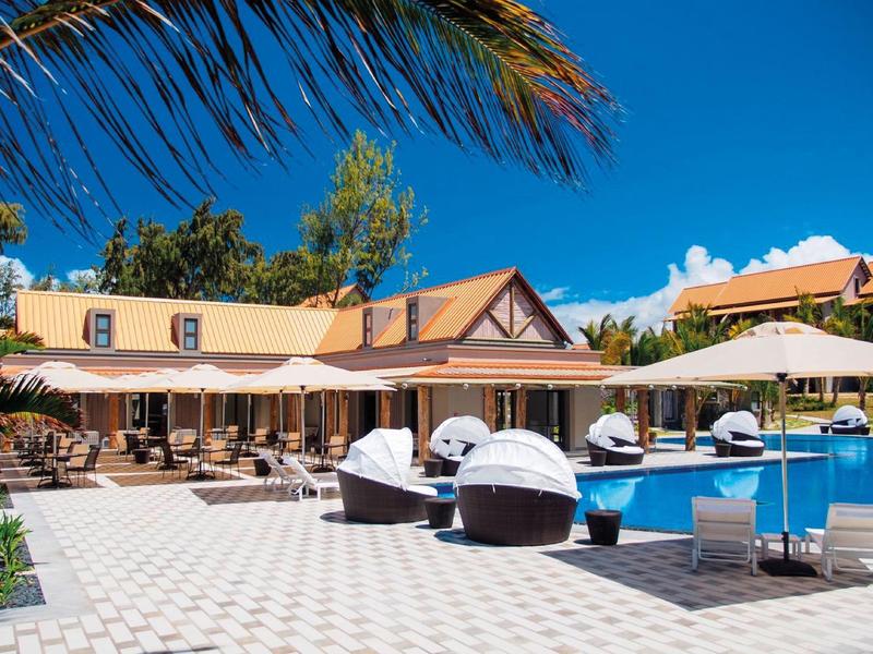 Resort zwembad met ligbedden, parasols en tropische palmbomen onder een heldere blauwe lucht.