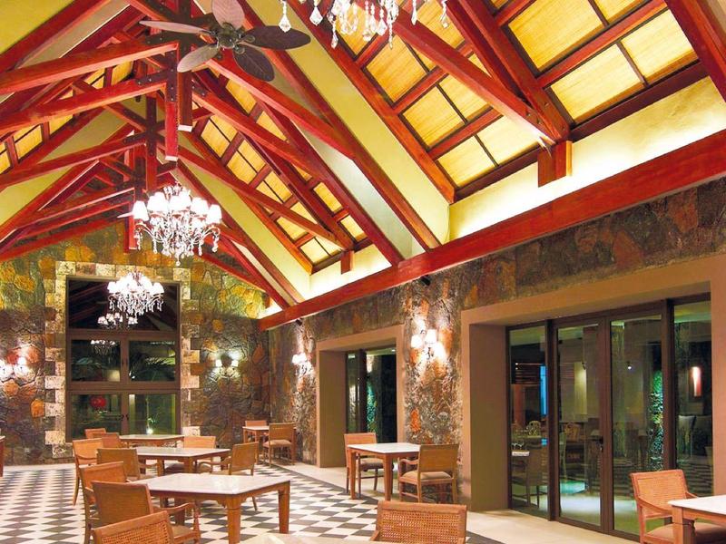 Ruime hotel eetzaal met houten stoelen, zwart-witte tegelvloer en kroonluchters onder een gewelfd plafond.