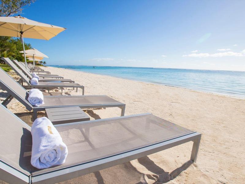 Strandstoelen met handdoeken en parasols langs een zandstrand onder een heldere blauwe lucht.