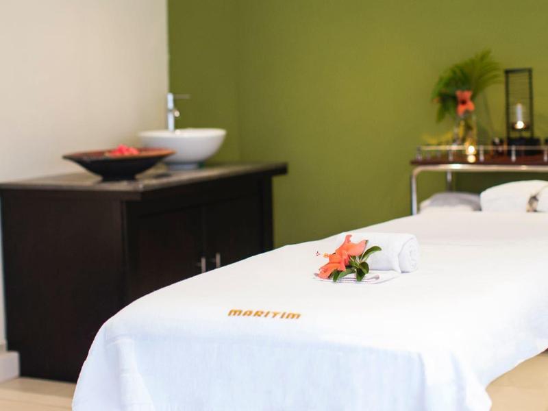 Massageruimte met een wit tafel, donkerhouten kast en ontspannende oranje bloemenaccenten.