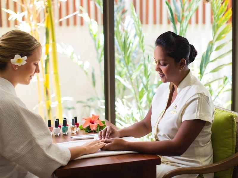 Twee vrouwen aan een tafel met nagellak, een krijgt een manicure in een spa-omgeving.