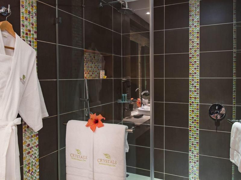 Moderne badkamer met zwarte tegels, witte badjassen, handdoeken en glazen douchedeur met mozaïek accenten.