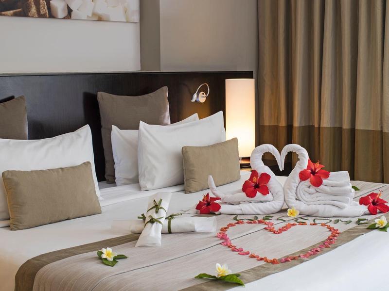 Hotelkamer met een netjes opgemaakt bed, handdoekzwanen, bloemversiering en warm licht.