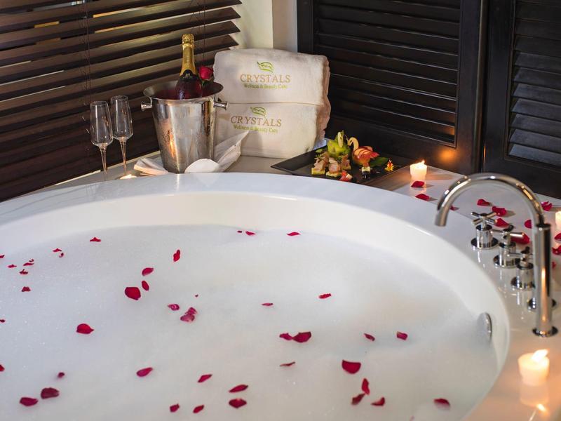 Rond bad gevuld met melkachtig water en rozenblaadjes, met wijnglazen en bloemen ernaast.