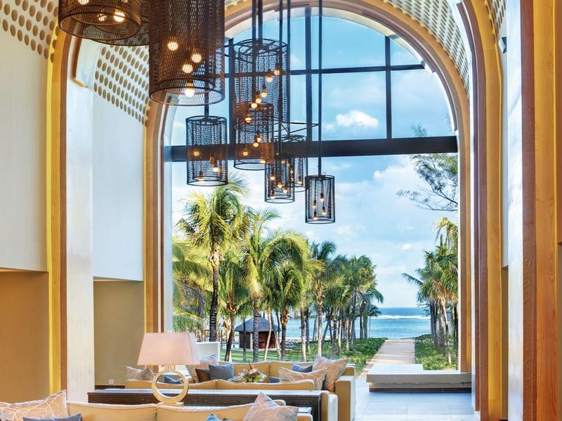 Luxuriöser Lounge-Bereich mit cremefarbenen Sofas, Holzbögen und Blick auf Palmen und Meer.