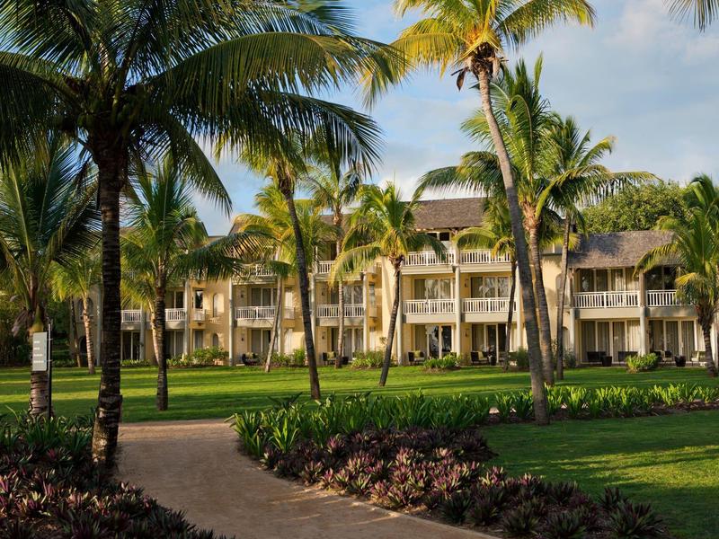 Große weiße Gebäude mit Balkonen, umgeben von grünen Palmen und gepflegten Rasenflächen.