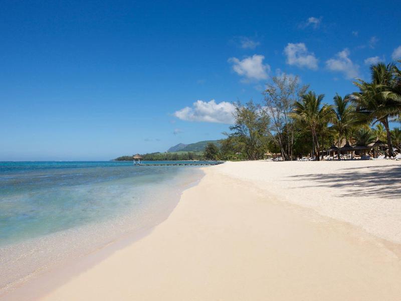 Ein leerer Sandstrand mit klarem Wasser, Palmen und blauem Himmel mit wenigen Wolken.
