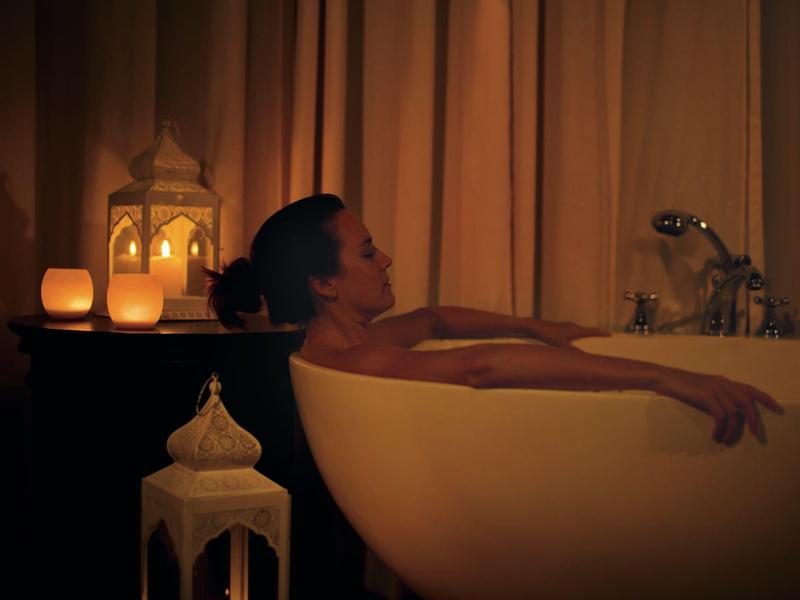 Eine Frau entspannt sich in einer Badewanne, umgeben von warmem Kerzenlicht und Vorhängen.