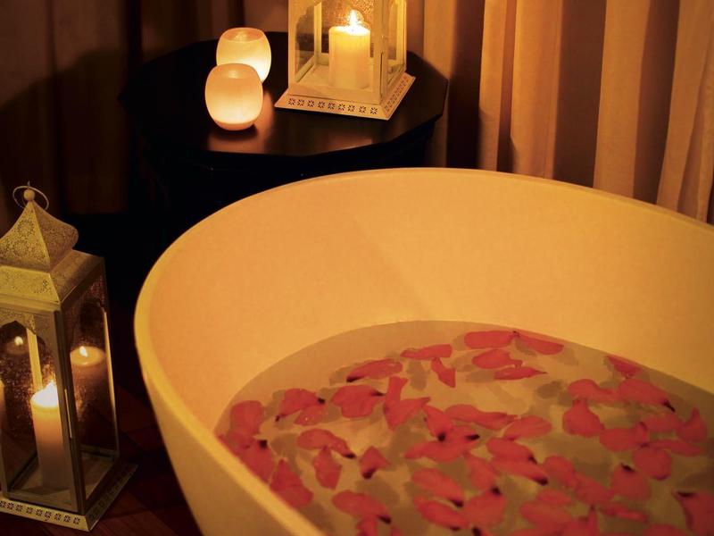 Weiße Badewanne mit Wasser, das mit bunten Blüten bedeckt ist, warm beleuchtet in dunklem Raum.