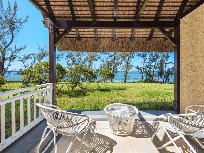 Terrasse mit weißen Stühlen, Holzdach und Blick auf grüne Wiese und Wasser im Hintergrund.