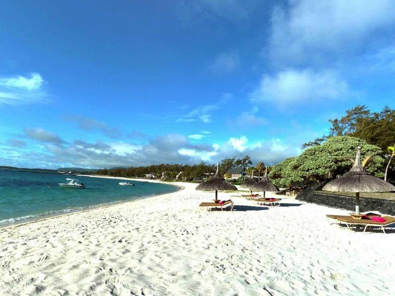 Spiaggia di sabbia bianca con sedie a sdraio, cielo azzurro limpido e hotel sul mare.