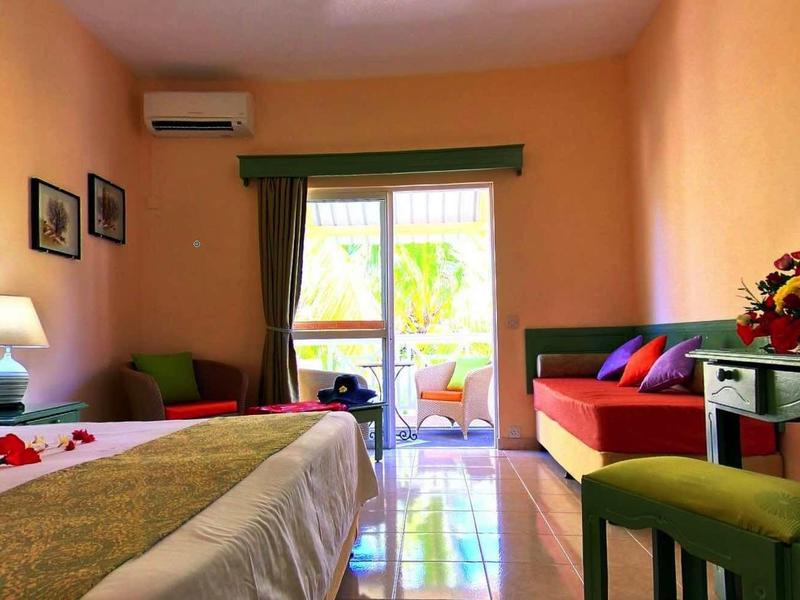 Camera d'hotel accogliente con letto, zona salotto e balcone, illuminata caldamente in arancione.