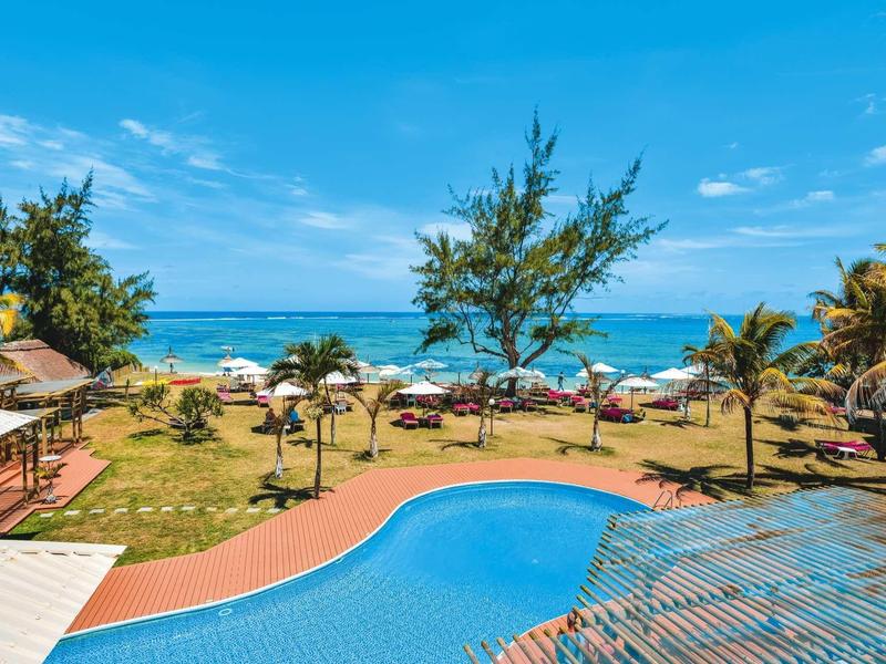 Piscina dell'hotel con vista sul giardino e sull'oceano sotto un cielo azzurro.