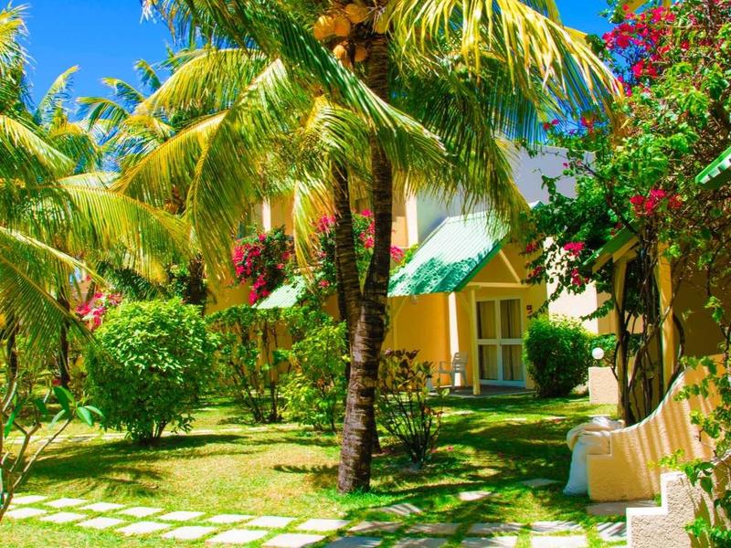 Giardino dell'hotel con palme, prati verdi e fiori colorati sotto un cielo azzurro.