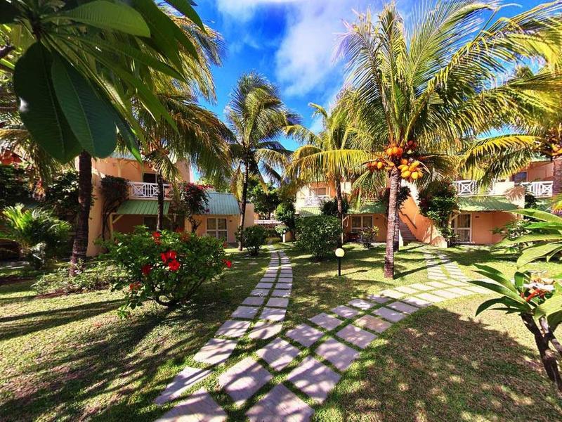 Sentiero attraverso un giardino tropicale con palme e sole vicino agli edifici dell'hotel.